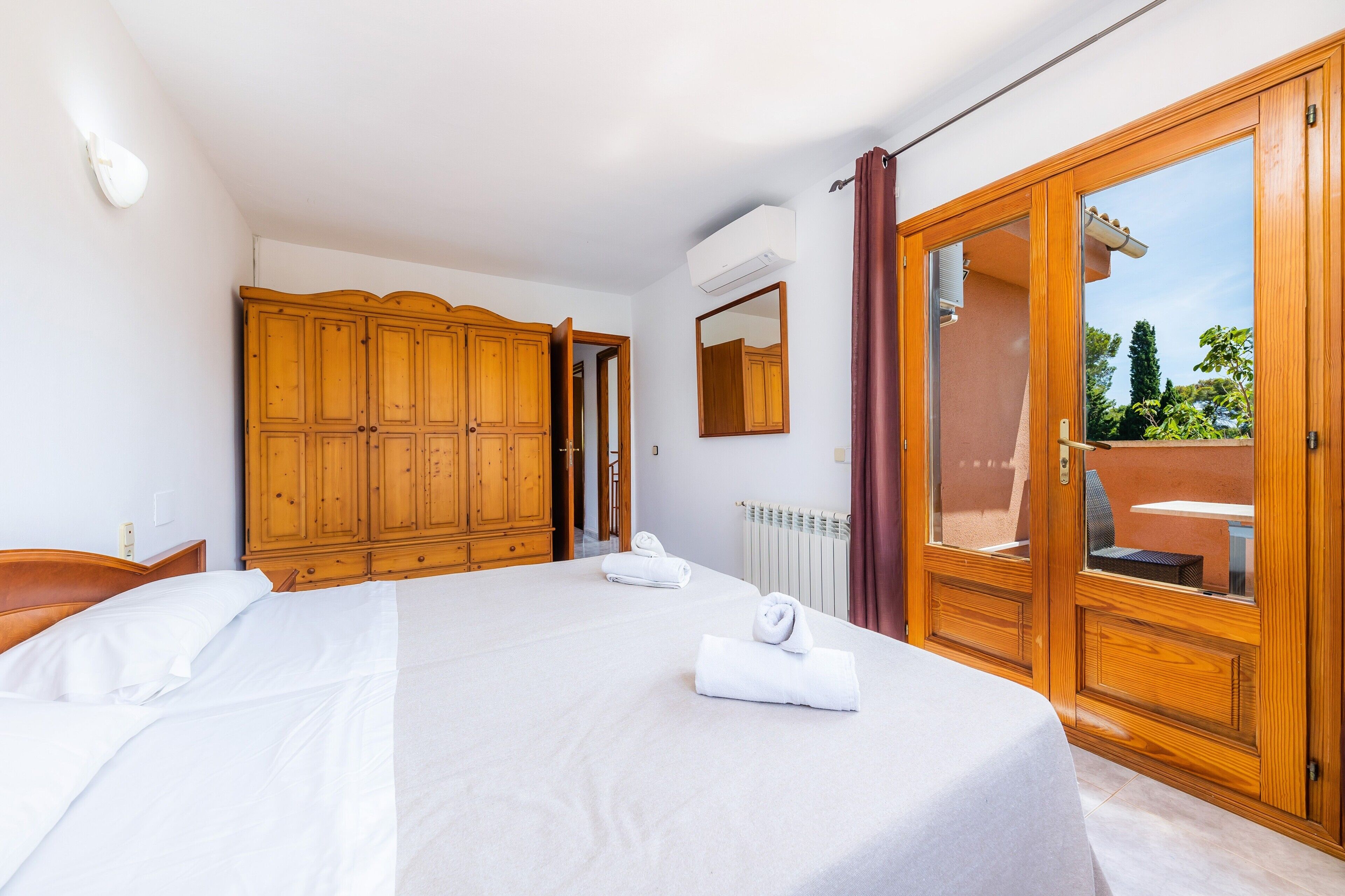 Ein Schlafzimmer mit Bett, Holzschrank, Spiegel und einer Schiebeglastür zum Außenbereich.
