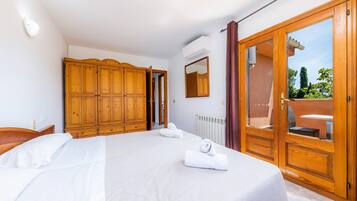 Ein Schlafzimmer mit Bett, Holzschrank, Spiegel und einer Schiebeglastür zum Außenbereich.