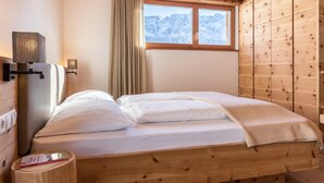 Ein raumförmiger Raum mit Holzbalken, einem Bett, einem Fenster mit Bergblick, einer Lampe und einem Nachttisch.