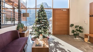 Ein modernes Interieur mit Weihnachtsbaum, einer Couch, einem Tisch mit Snacks und Blick auf Berge durch große Fenster.