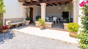 Un espacio de estar al aire libre cubierto con bancos de piedra y plantas en macetas, que conduce a un edificio con techo de tejas y columnas.