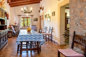 A dining area with a table set for four, wooden chairs, a chandelier, and a stone wall.