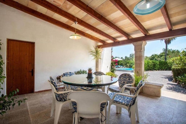 An outdoor patio with a round table and chairs, a wooden ceiling, and a view of a swimming pool.