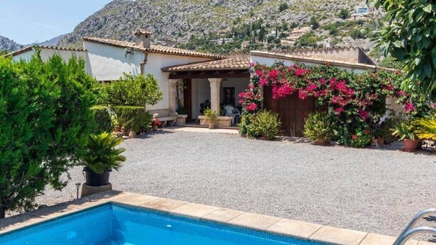 Un área de piscina con vista despejada del paisaje circundante, incluyendo un edificio con techo de tejas y un camino de grava.