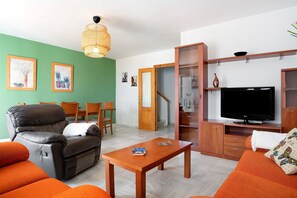 A living room with a leather sofa, a wooden coffee table, a television, and a dining area with chairs and a table.