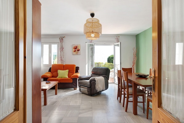 A living room with a sofa, armchair, dining table, and chairs.