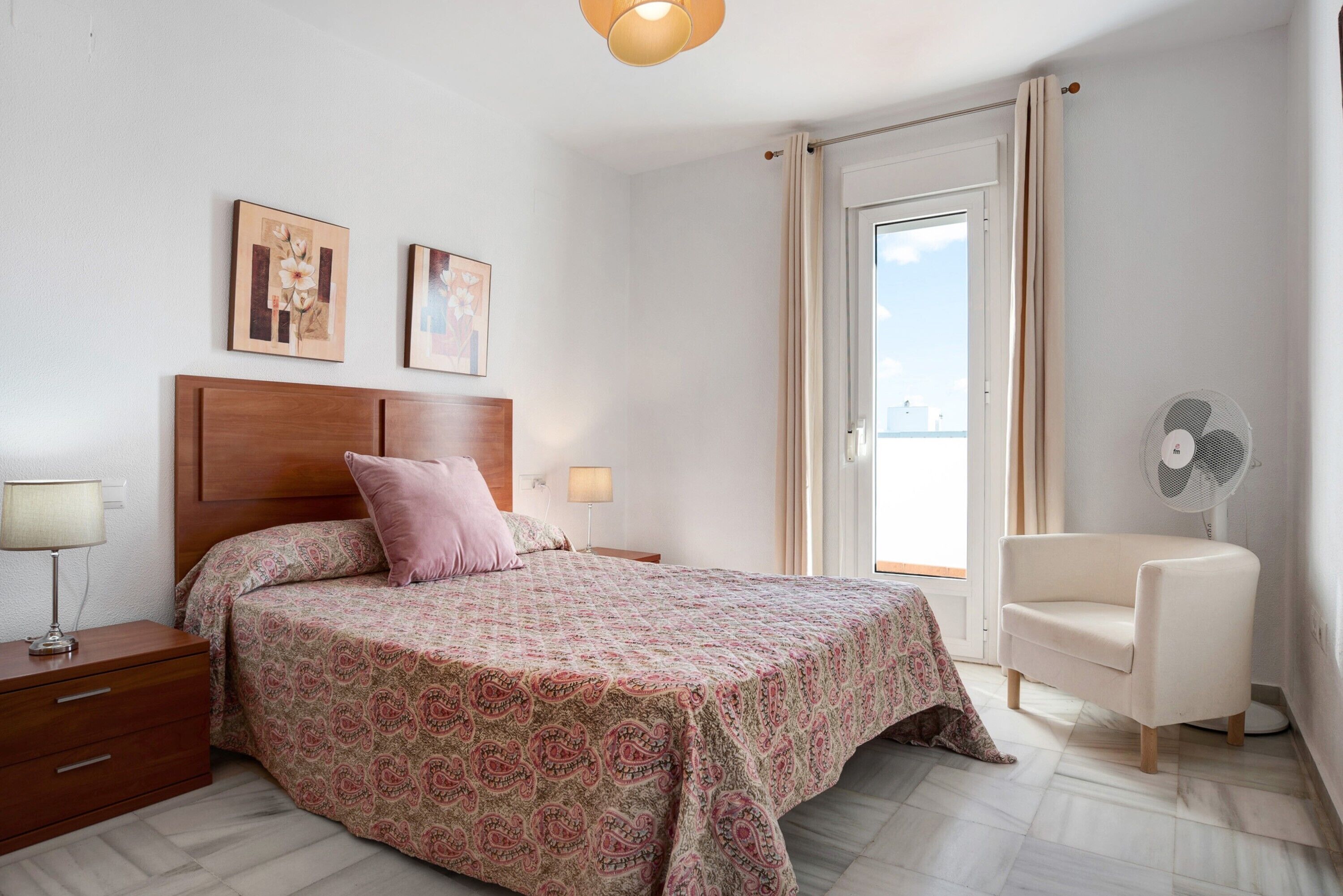 Ein Schlafzimmer mit einem Bett, Nachttischen, einem Sessel und einem Fenster.