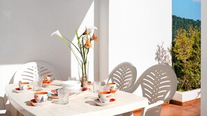 Een tafel gedekt met witte en oranje bekers, een glazen vaas met bloemen, en stoelen met bladmotieven.