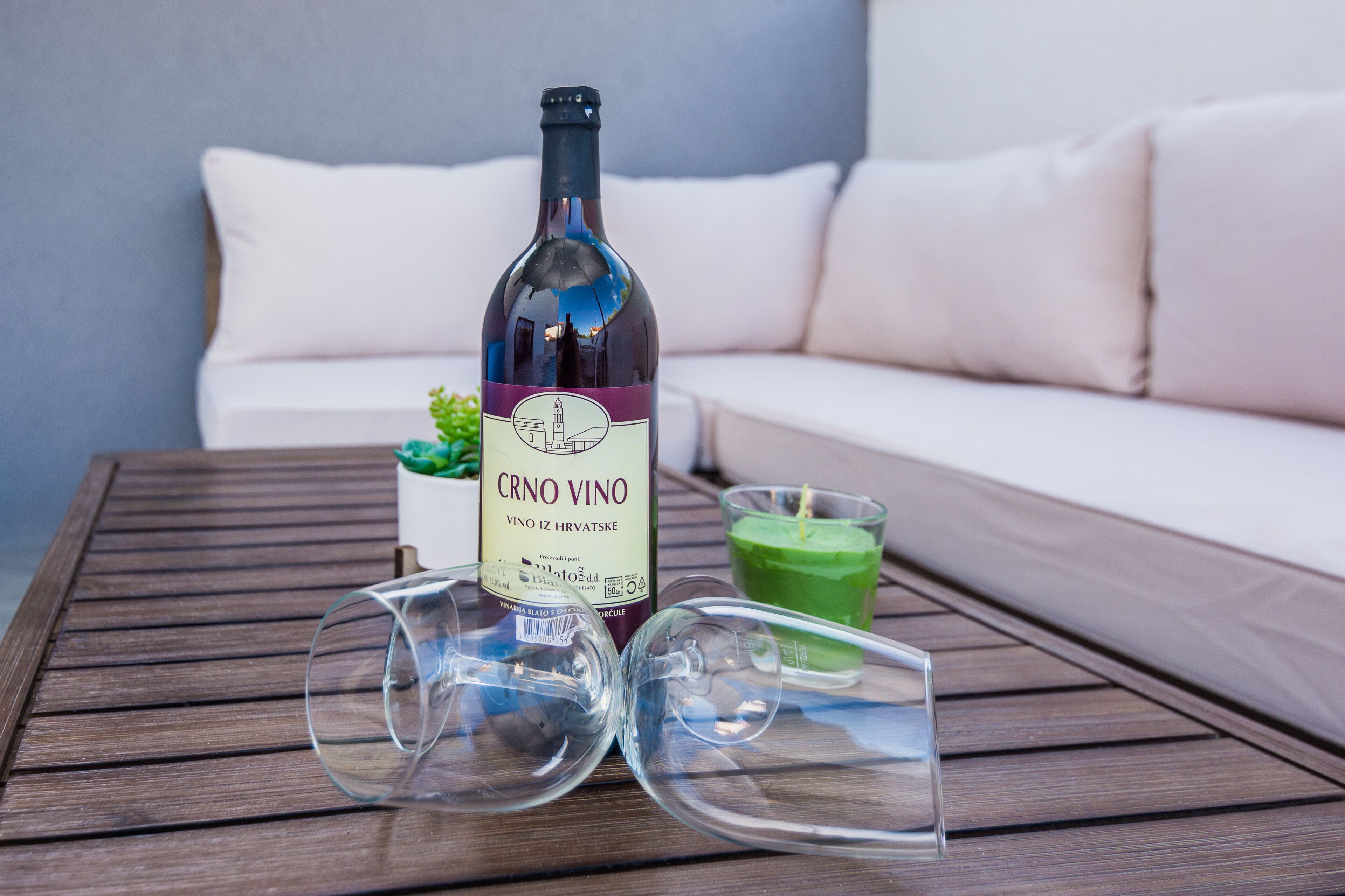 A bottle of CRNO VINO wine, two empty wine glasses, and a green candle on a wooden table.