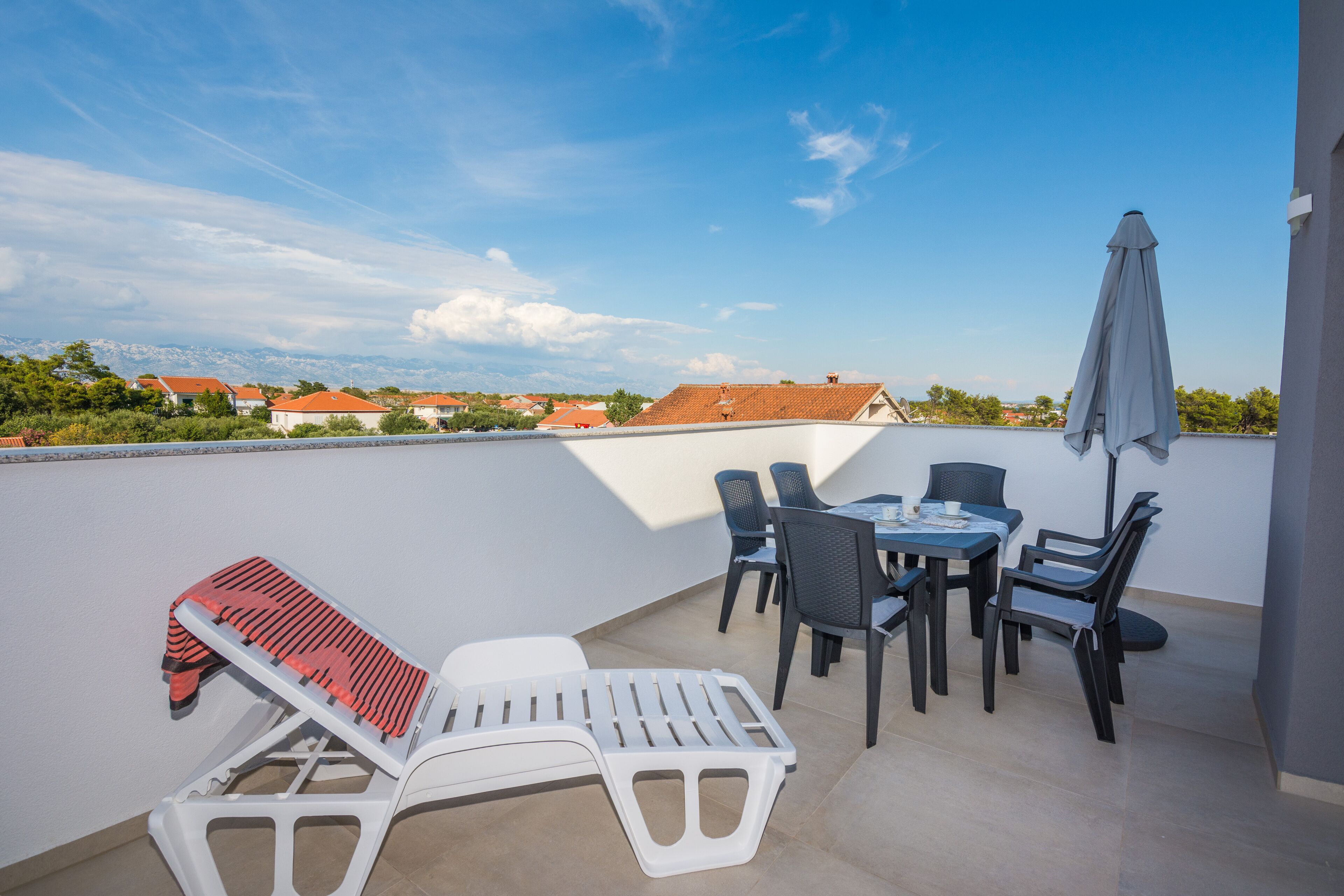 A rooftop terrace with a table and chairs, a sun lounger, and a view of the cityscape.
