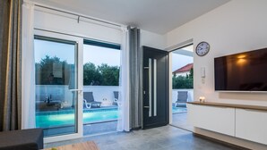 A modern living room with a pool view, sliding glass doors, a flat-screen TV, and a minimalist design. - Apartment Spanic 2 (Vir)