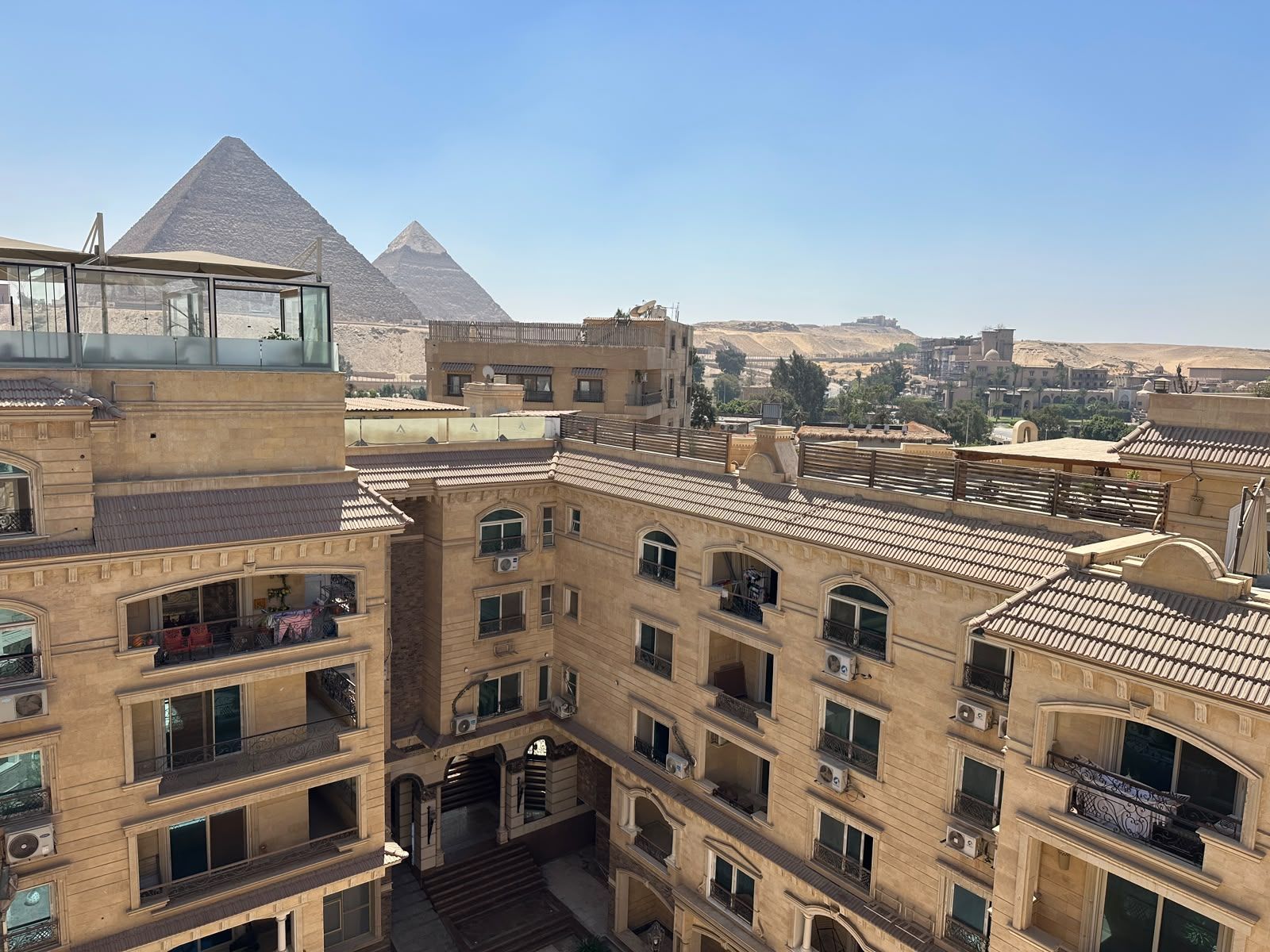 A multi-story building with balconies and a view of the pyramids in the background.