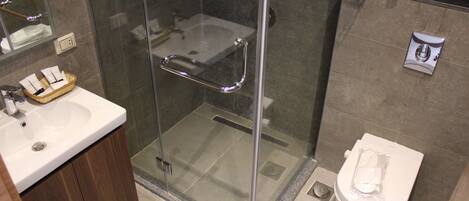 A modern bathroom with a glass-enclosed shower, a white sink with a wooden cabinet, and a toilet with a paper towel dispenser.