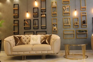 Una sala de estar moderna con un sofá color crema, una mesa redonda con marco dorado y estantes fijos en la pared con diversos objetos decorativos.