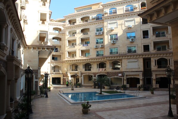 A courtyard with a swimming pool, surrounded by multi-story buildings with balconies and air conditioning units. - Jasmine Pyramids Hotel  (Giza)