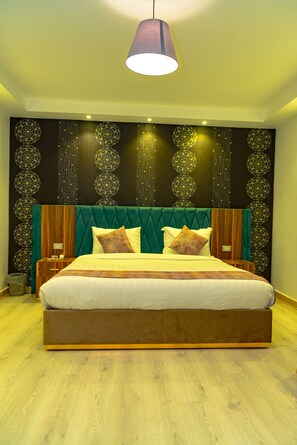 A large bed with a wooden frame and green upholstered headboard, a hanging pendant light, and a wall with decorative patterns. - Jasmine Pyramids Hotel  (Giza)