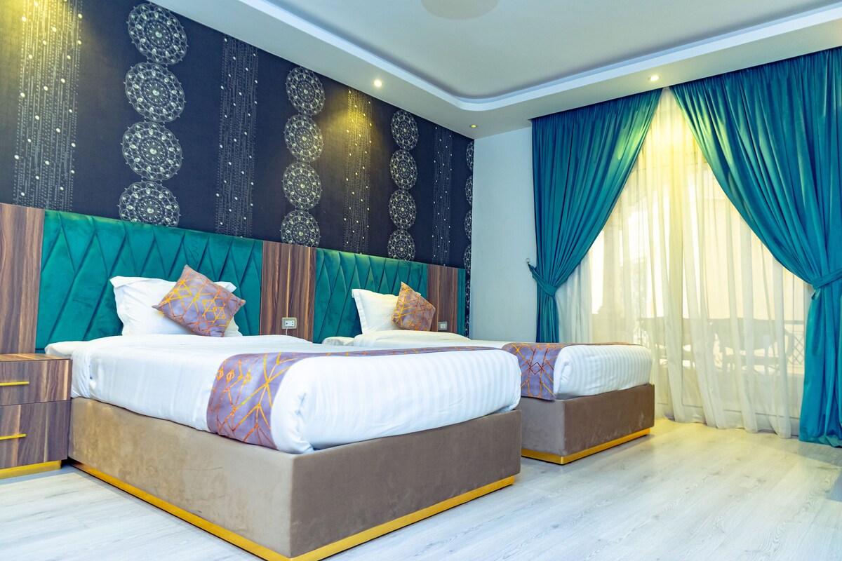 Una habitación de hotel moderna con dos camas grandes, un muro decorativo y un ventanal con cortinas.