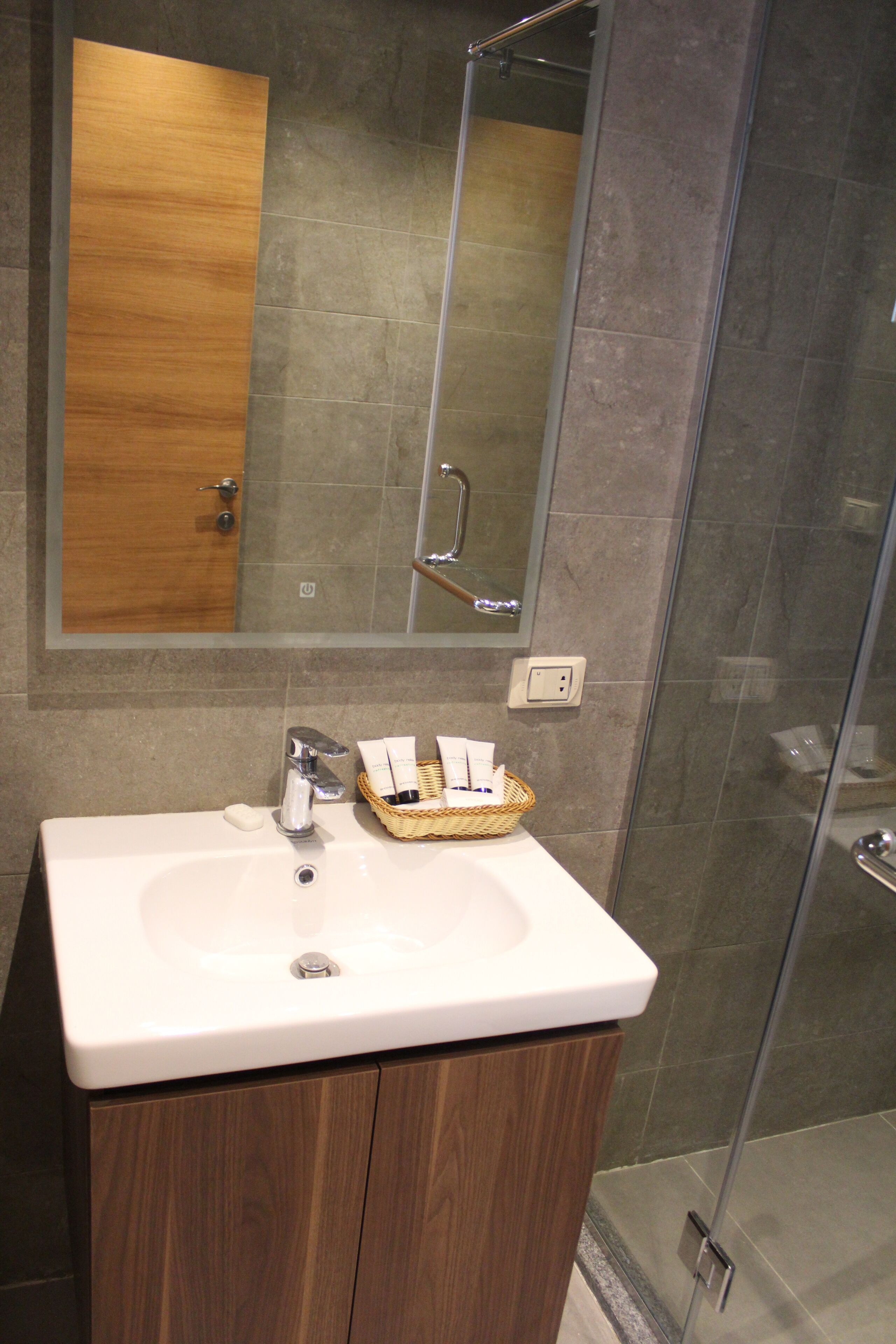Une salle de bain avec un meuble-lavabo en bois, un lavabo blanc, un miroir et une cabine de douche en verre.