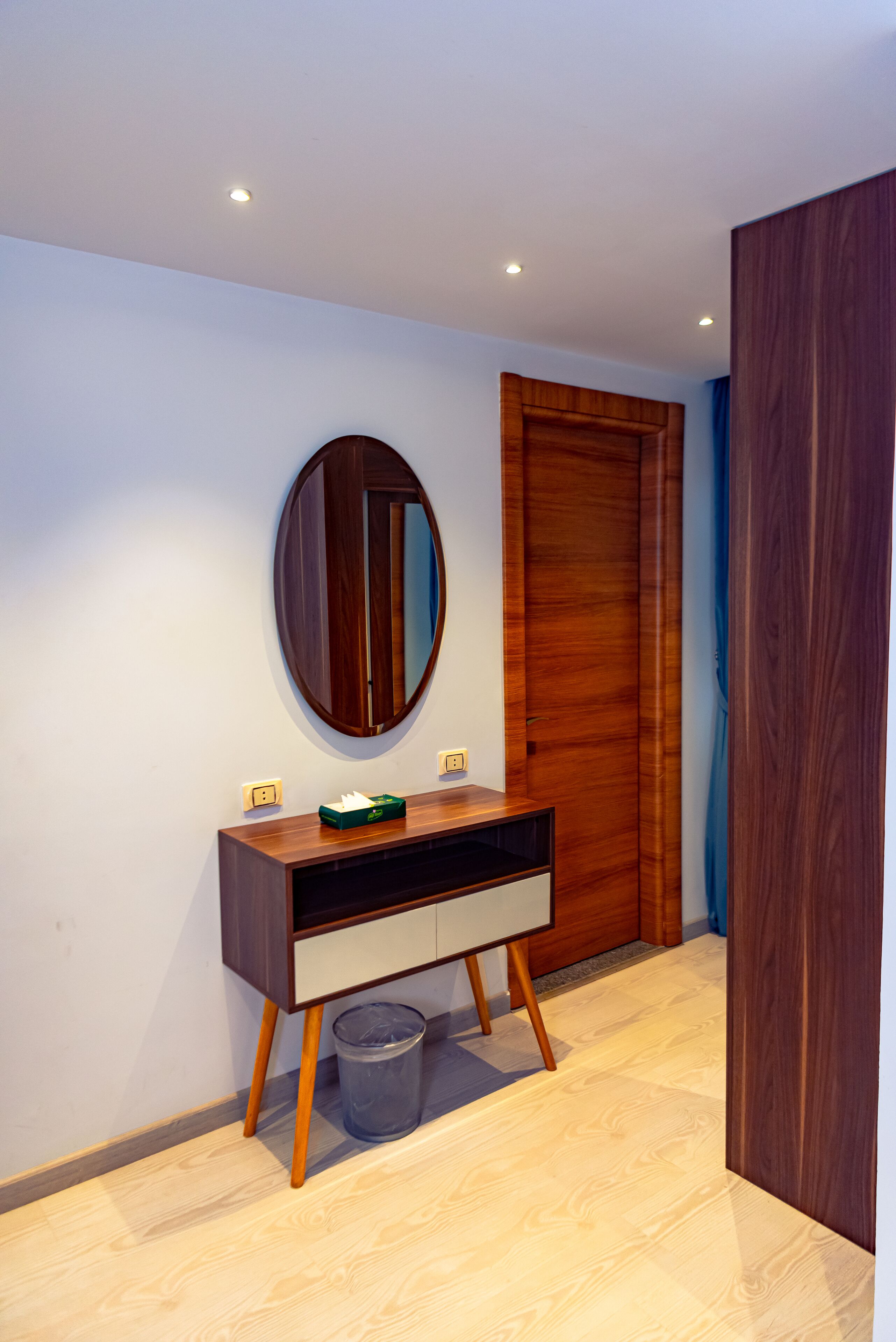 Un baño moderno con un tocador de madera, un espejo redondo y una puerta de madera.