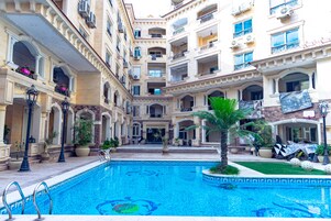 Un hôtel à plusieurs étages doté d’une cour intérieure où se trouvent une piscine, des plantes en pot et des espaces de détente en plein air.