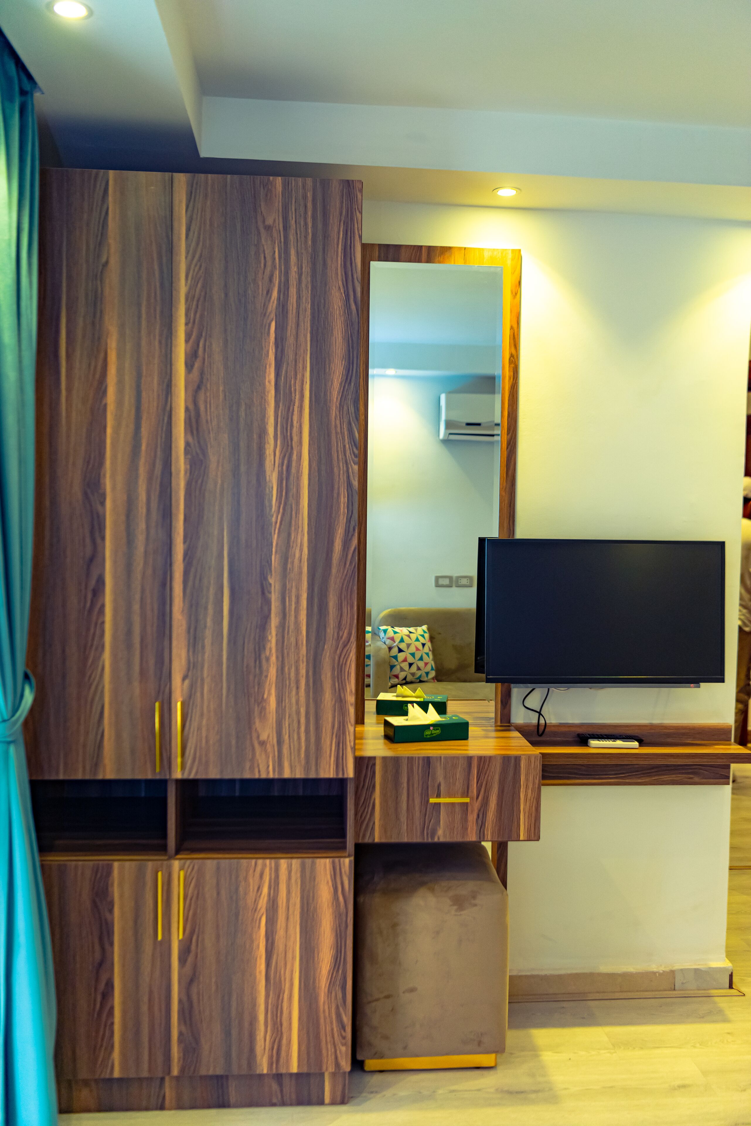 A modern living room with a large wooden wardrobe, a flat-screen TV, and a small table with a remote control.