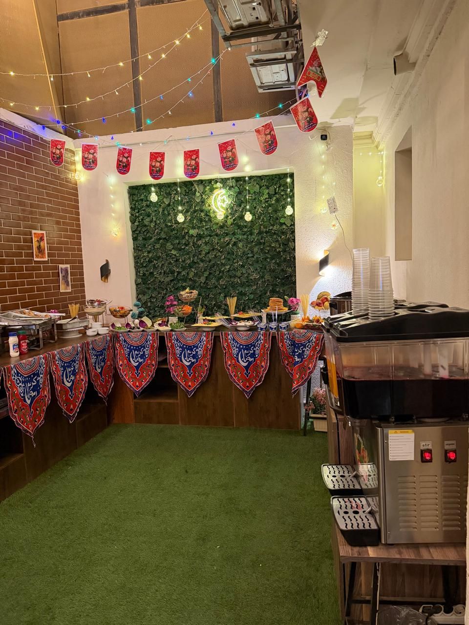 Ein Buffet mit Grünwand im Hintergrund, Lichterketten und einer Kaffeemaschine.