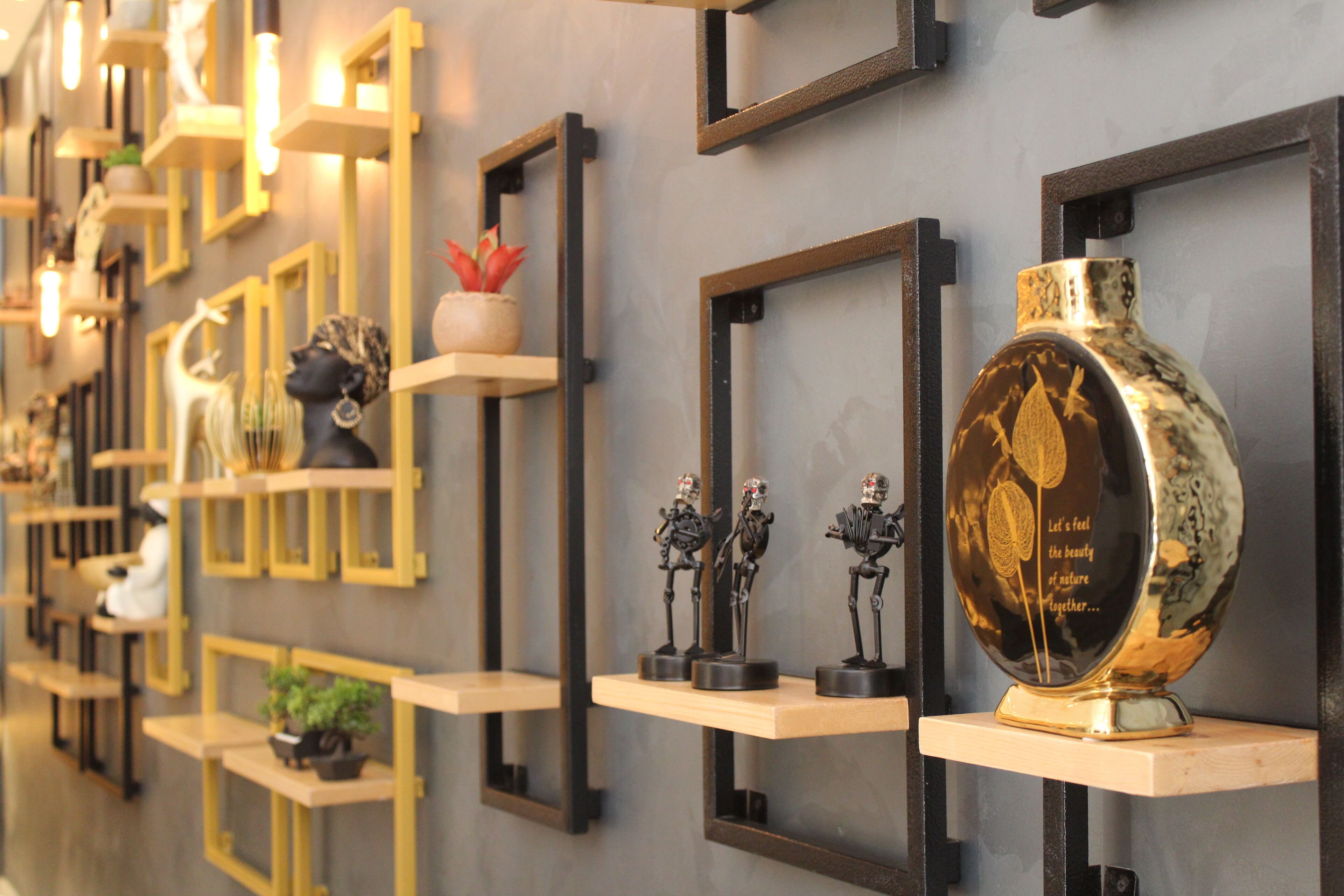 Pared decorada con diversos objetos, incluyendo cuadros enmarcados, esculturas y un jarrón grande con superficie reflectante.