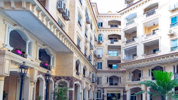 Un área de piscina con un diseño geométrico, rodeada por un edificio de varios pisos con balcones y plantas en macetas.