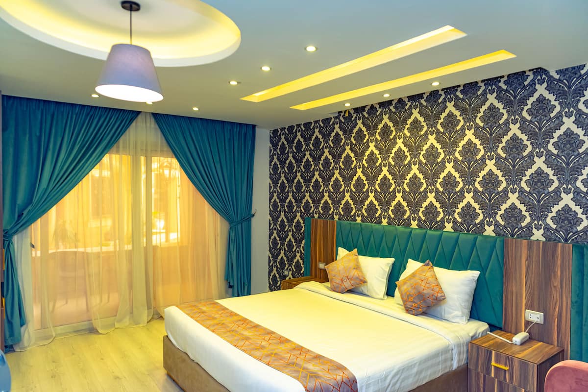 Habitación de hotel con una cama grande, una mesita de noche de madera, un cabecero tapizado en color verde azulado y un papel pintado estampado.