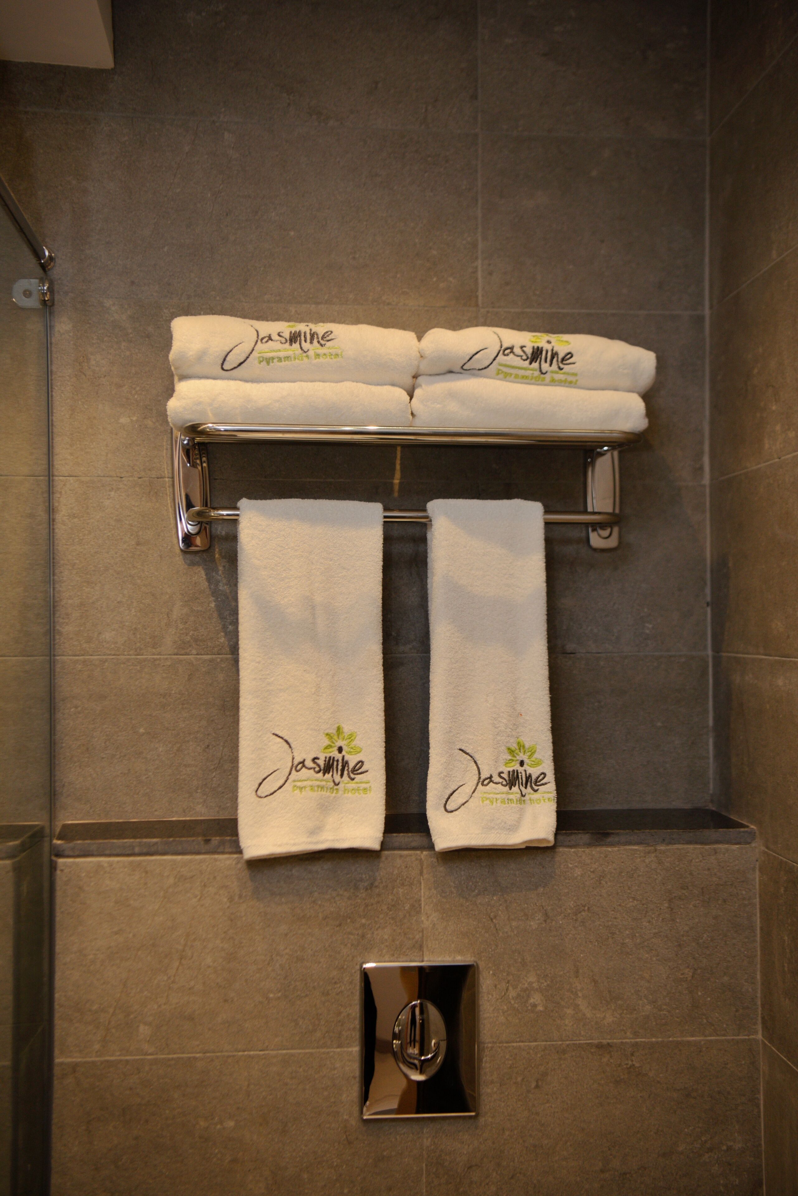 A bathroom with a towel rack holding three white towels with "Jasmine" branding.