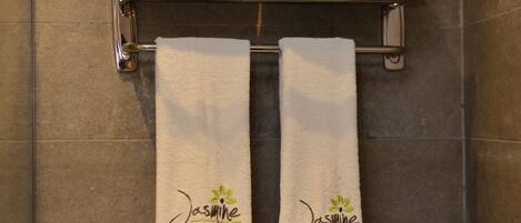A bathroom with a towel rack holding three white towels with "Jasmine" branding.