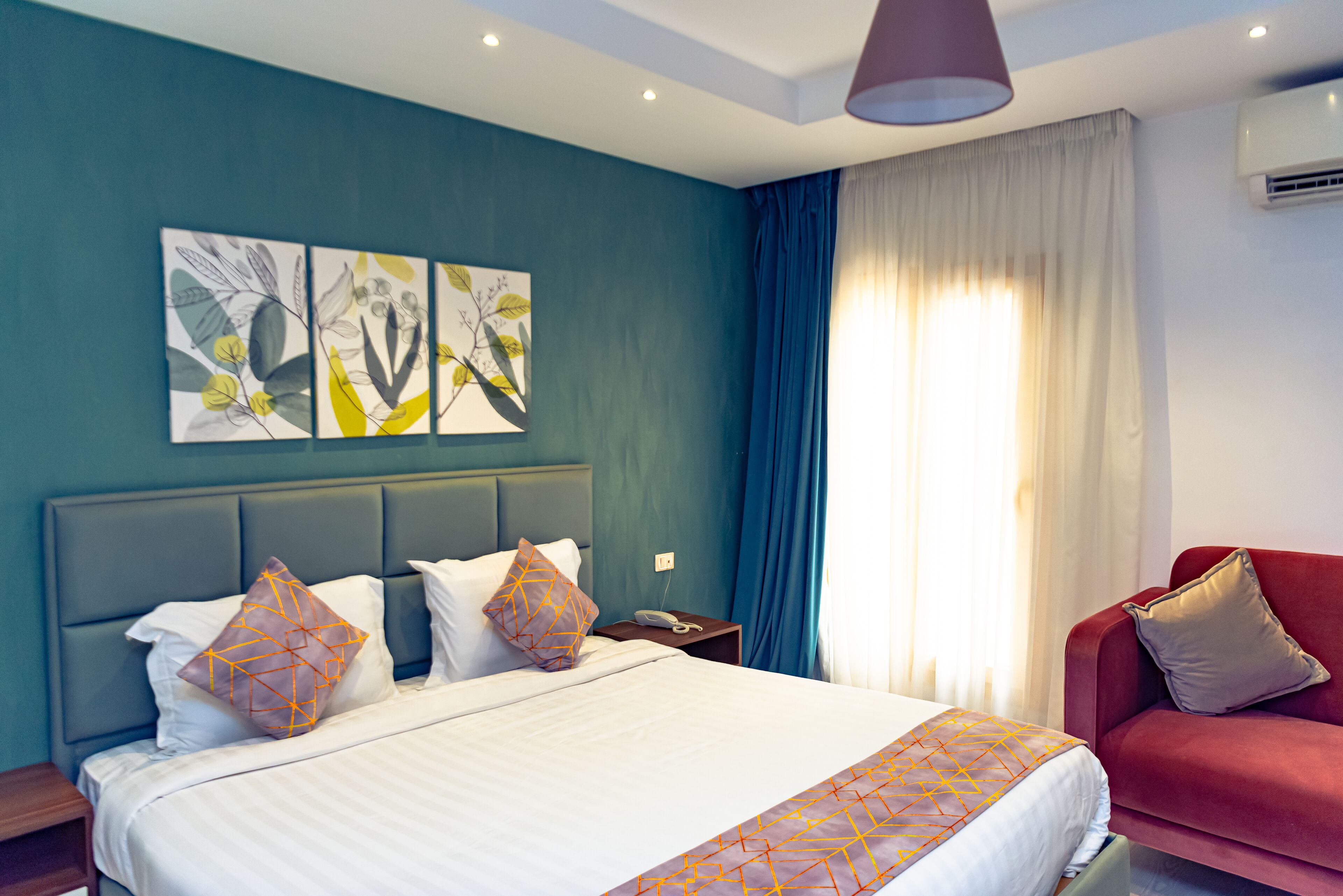 A hotel room with a bed, a red sofa, and a nightstand.