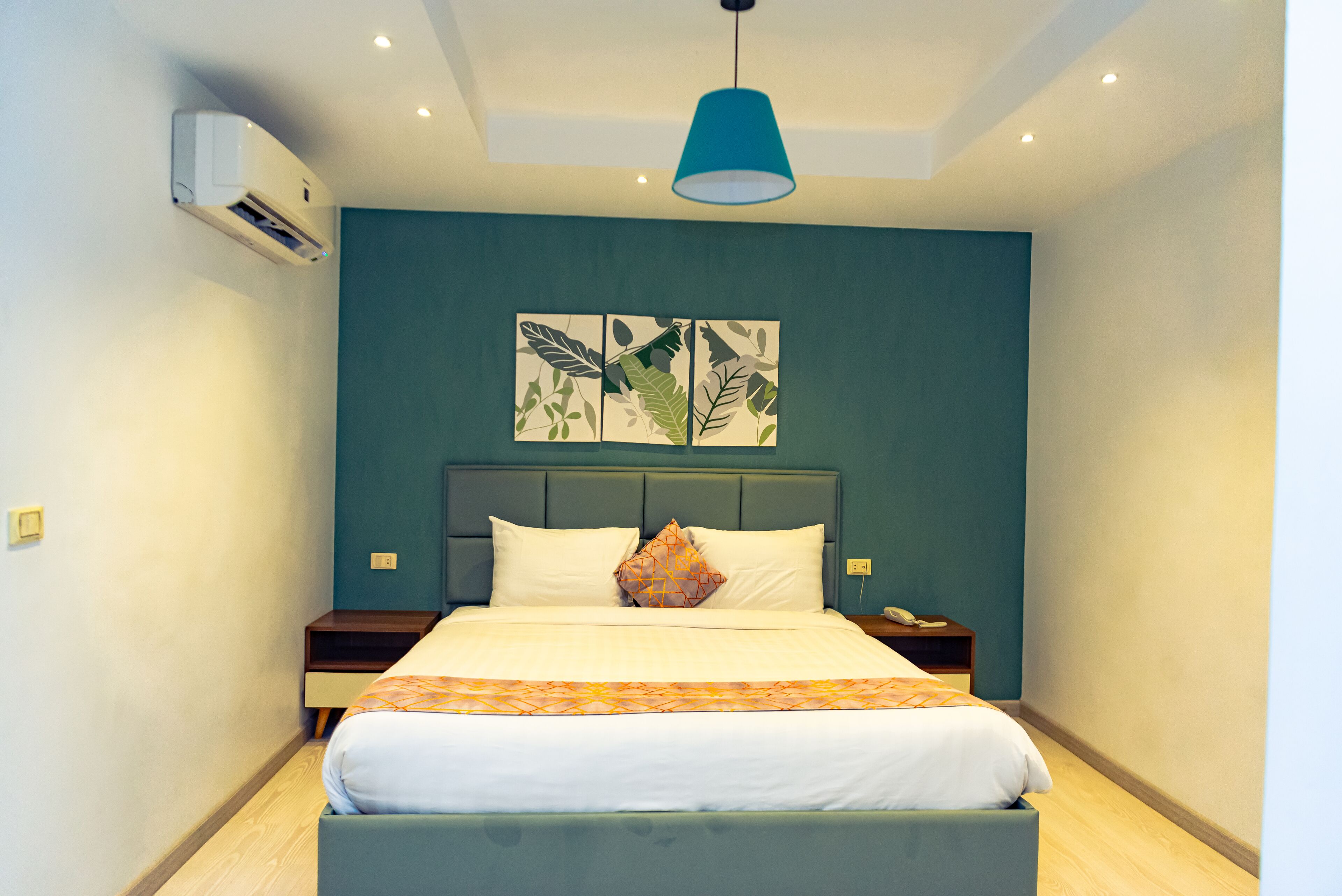 A neatly made bed with a patterned bedspread, a single pillow, and a bedside table with a lamp.