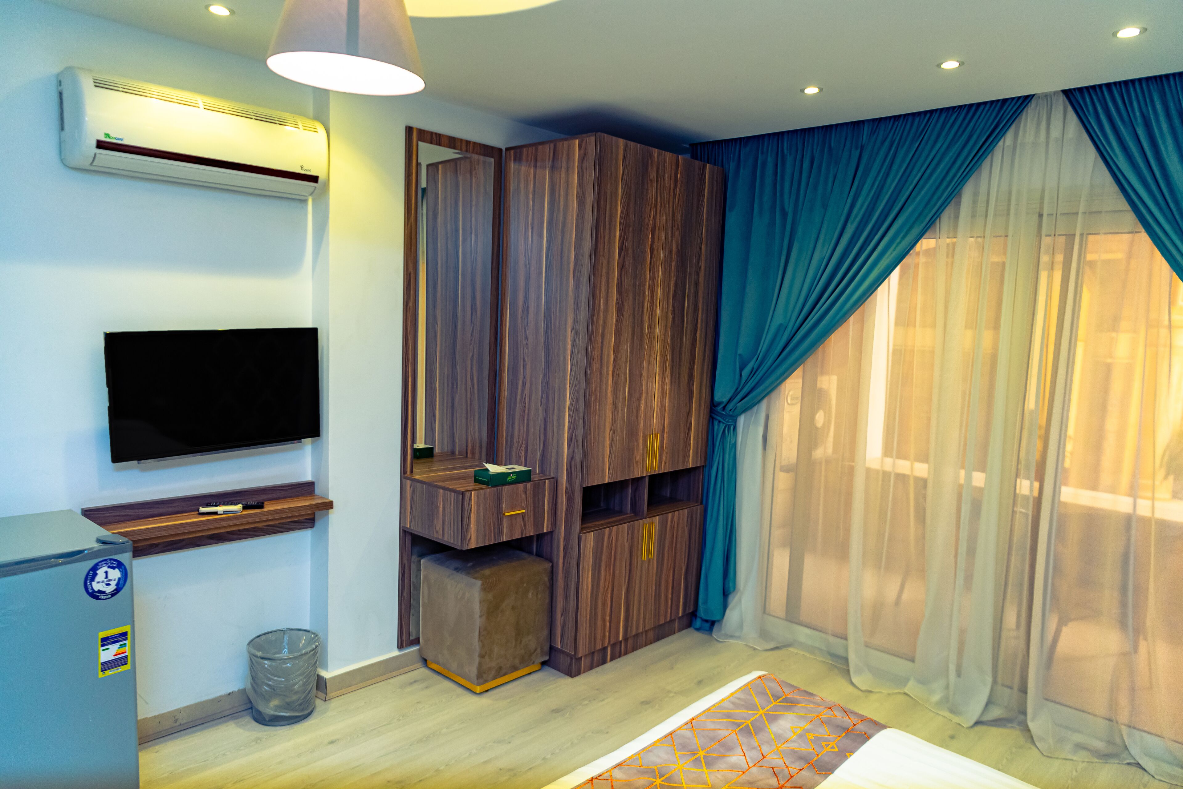 Un dormitorio moderno con televisor integrado, armario y un ventanal con cortinas de gasa.