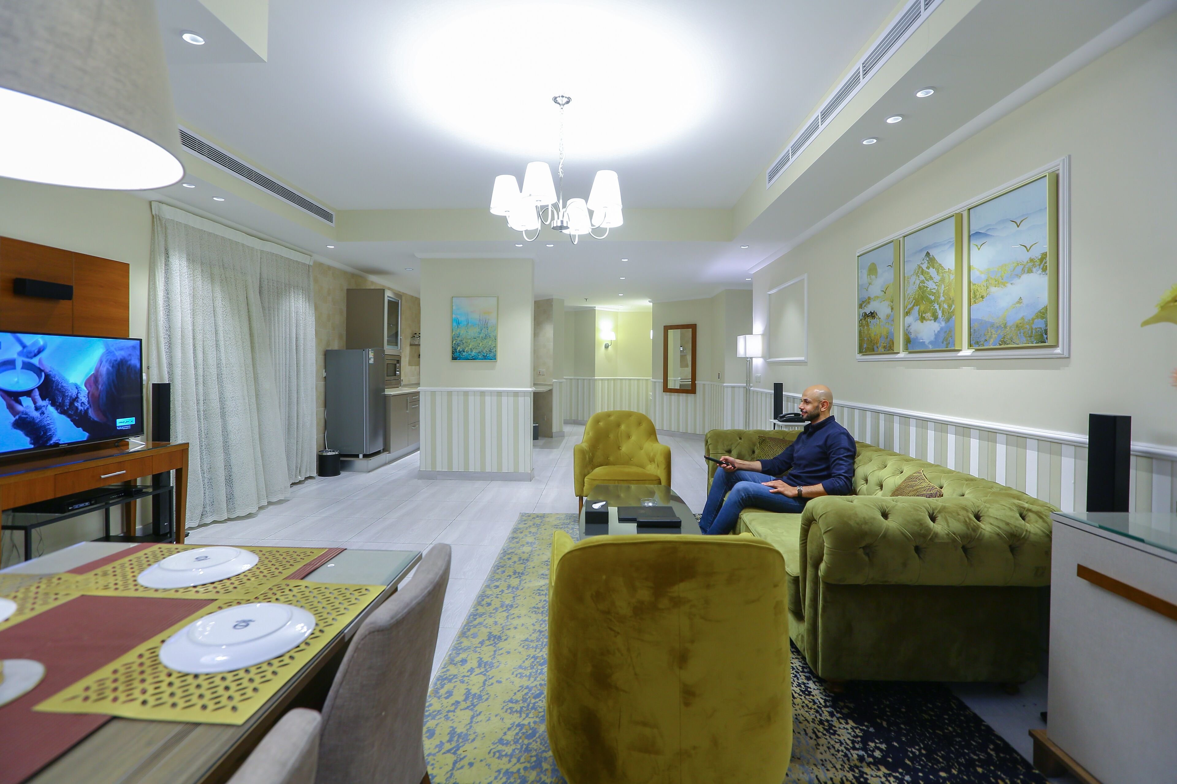 Un hall d’hôtel comprenant un espace repas, un téléviseur, un lustre et des œuvres d’art accrochées aux murs.