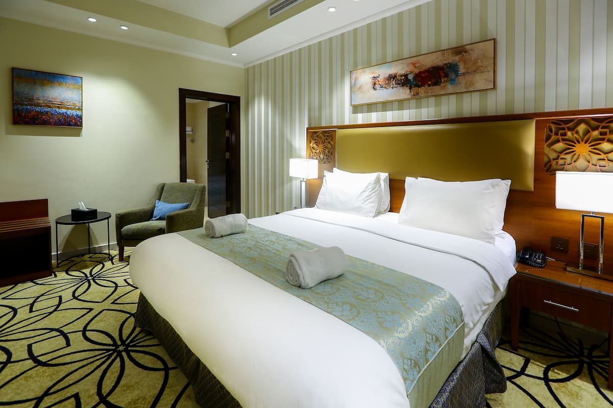 A hotel room with a large bed, a chair, a desk, and a lamp.