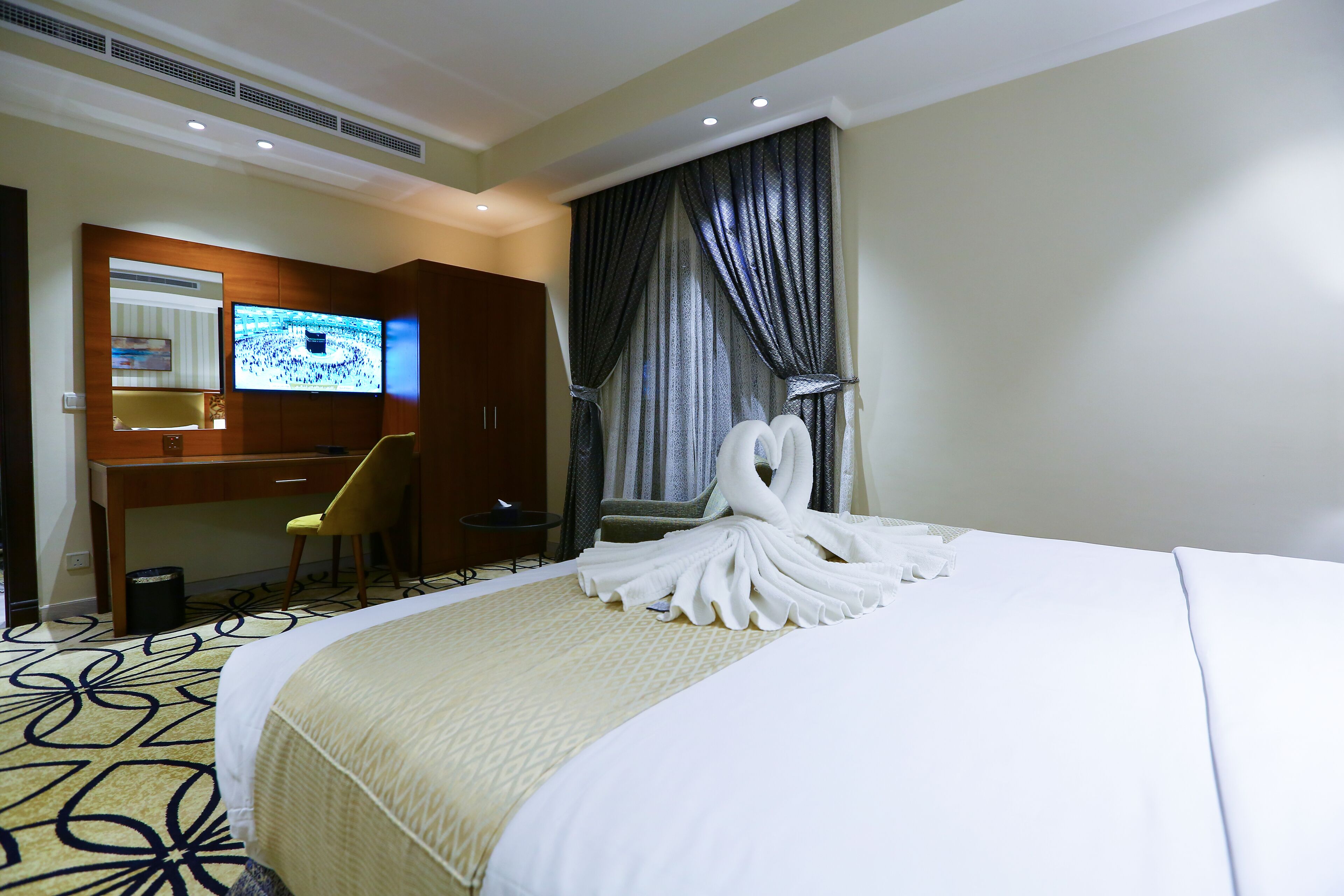 A hotel room with a large bed, a desk with a chair, a television, and a window with curtains.