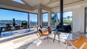 Un salón amplio con un ventanal grande con vistas a un paisaje urbano, una chimenea y muebles modernos.