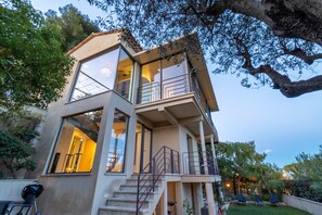 A modern two-story house with large windows, a balcony, and a well-maintained garden.