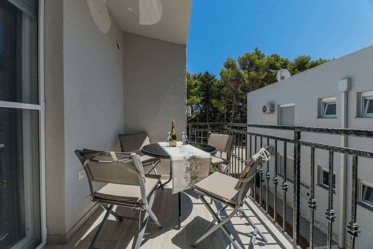 Un balcon avec une table et des chaises, une bouteille de champagne et une vue sur les arbres et les bâtiments.