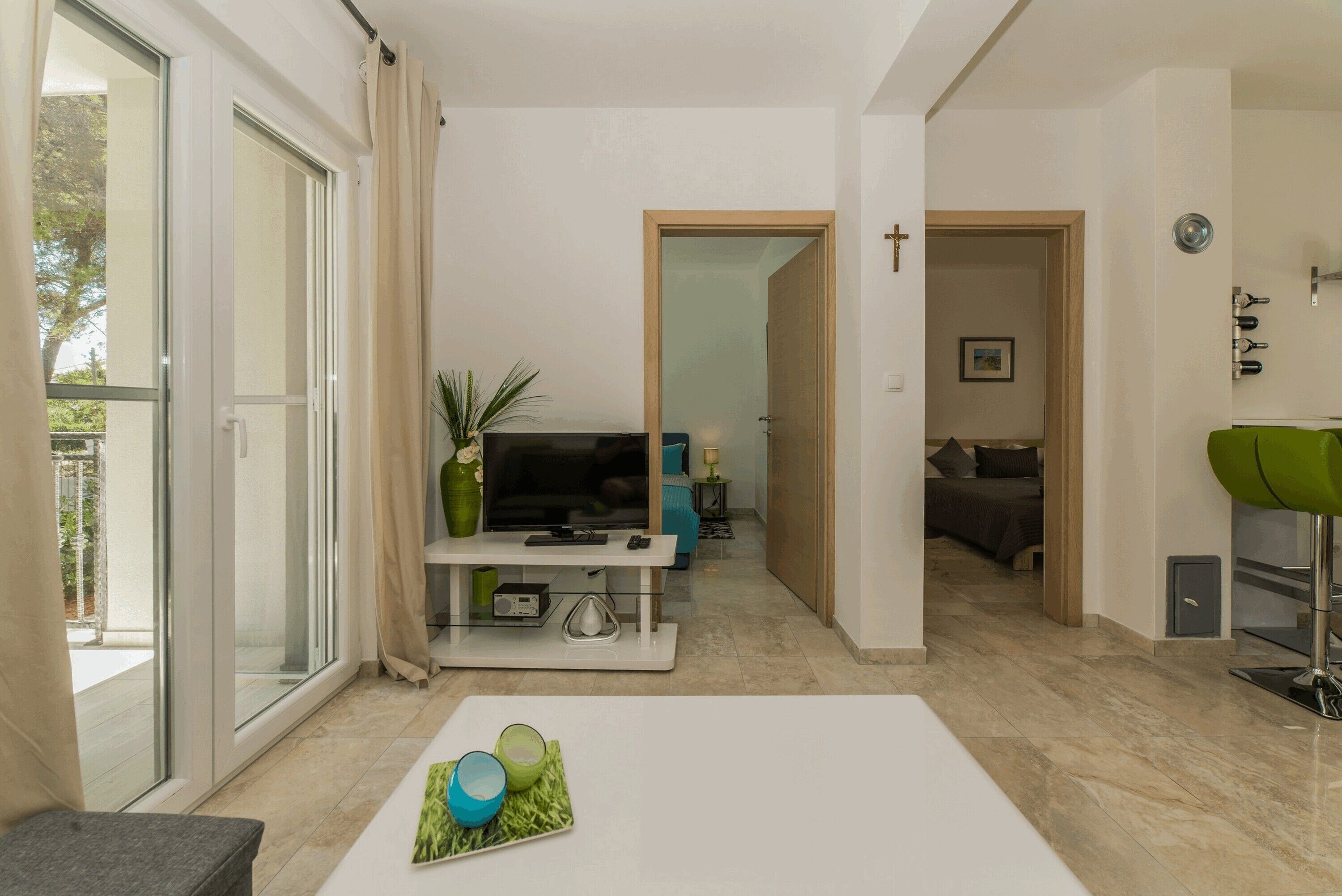 A modern living room with a white sofa, a coffee table with decorative items, a TV, and a sliding glass door leading to an outdoor area.