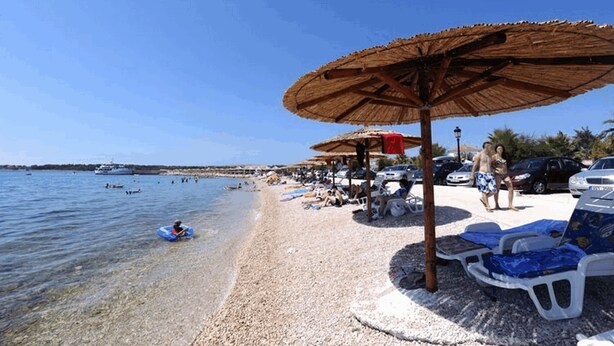 A beach with umbrellas, lounge chairs, and a clear blue sky. - Apartment Stichling (Vir)