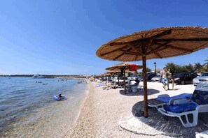 A beach with umbrellas, lounge chairs, and a clear blue sky. - Apartment Stichling (Vir)