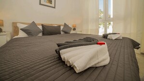 A neatly made bed with a dark quilt, pillows, and folded towels. - Apartment Stichling (Vir)