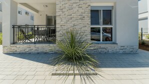 A modern building with a stone facade, a balcony with a metal railing, and a large plant in the foreground. - Apartment Stichling (Vir)