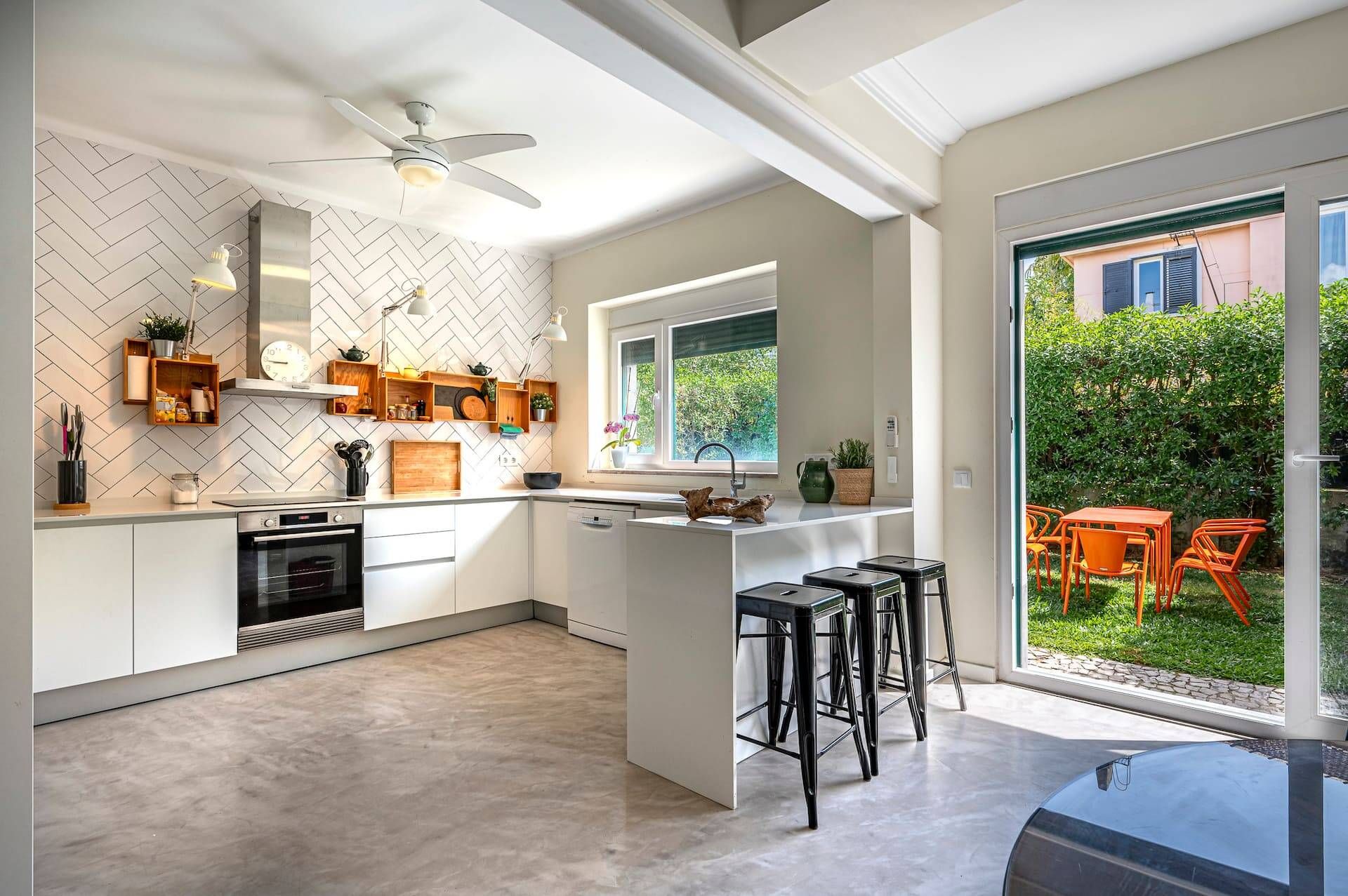 A modern kitchen with white cabinetry, a herringbone-patterned backsplash, and a central island with stools.