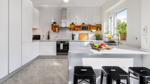 Eine moderne Küche mit weißen Schränken, einer zentralen Kochinsel mit Barhocker, einem eingebauten Backofen und einer Küchenrückwand mit Zickzackmuster.