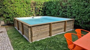 A wooden hot tub with a clear blue interior, surrounded by a grassy area and a stone pathway.