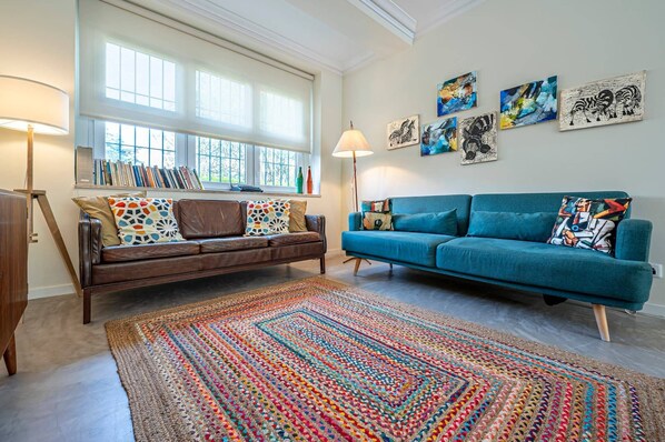 A living room with a brown leather sofa, a teal sofa, a colorful rug, and wall art.