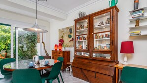 Ein Essbereich mit einem Glastisch, grünen Stühlen, einer Holzkabine mit Glastüren und einer roten Lampe.